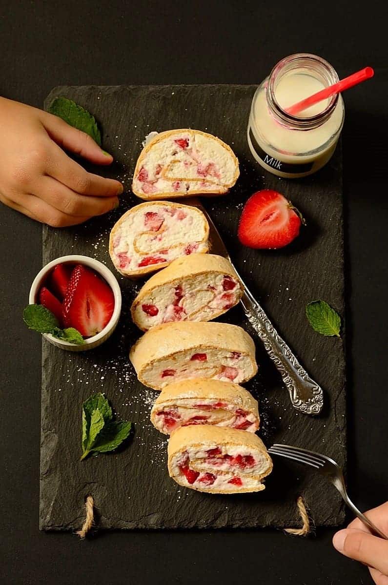 a hand reaches for sliced strawberry cream dessert