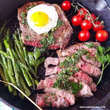 Bife a cavalo em uma frigideira com verduras do lado.