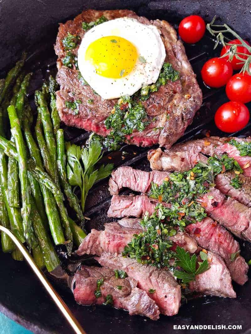 close up de bife a cavalo mal passado com vegetais em uma frigideira