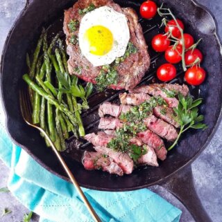 Steak and eggs in a pan with sauce on top and veggies on the side