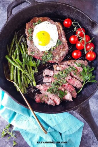 Steak and eggs in a pan with sauce on top and veggies on the side