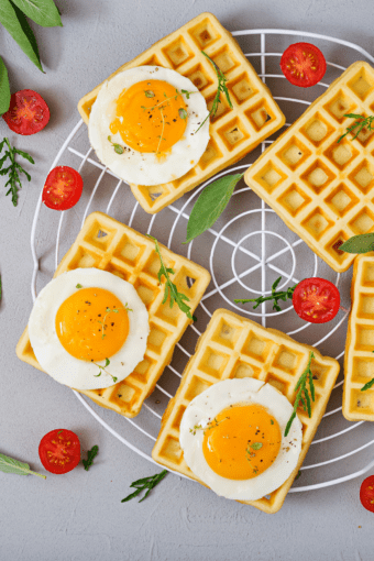 uma gradinha com waffle pão de queijo, ovos, tomates e ervas