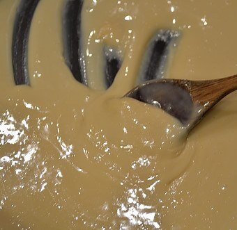 Sweetened condensed milk being combined with melted butter in a saucepan with a wooden spoon