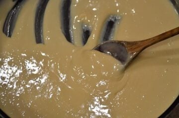 Sweetened condensed milk being combined with melted butter in a saucepan with a wooden spoon