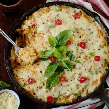 chicken pasta bake with bacon garnished on top with fresh tomatoes and basil leaves