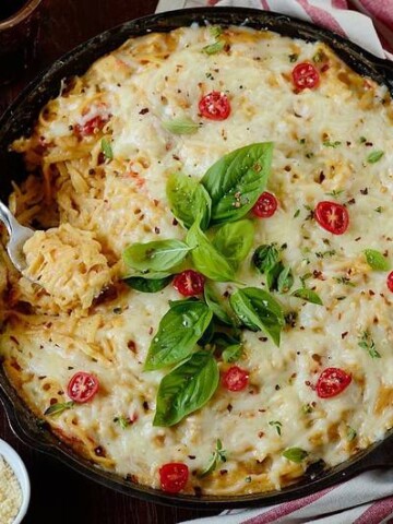 chicken pasta bake with bacon garnished on top with fresh tomatoes and basil leaves