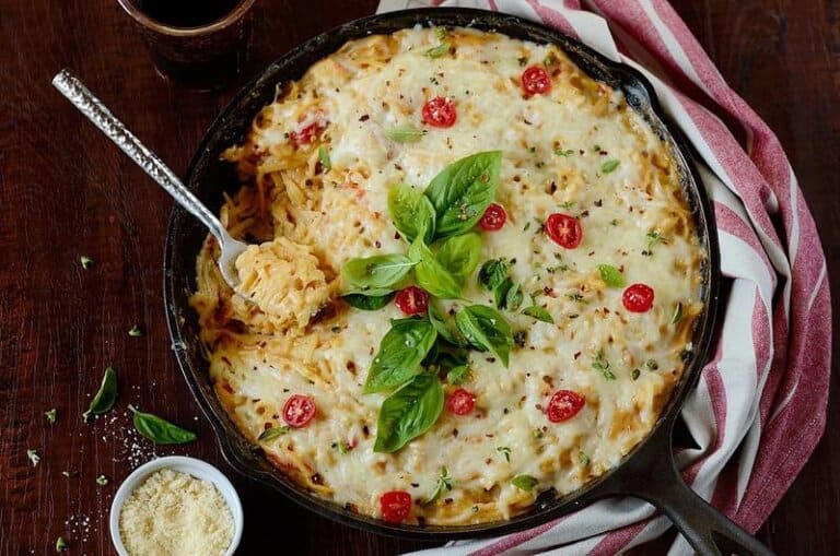chicken pasta bake with bacon garnished on top with fresh tomatoes and basil leaves