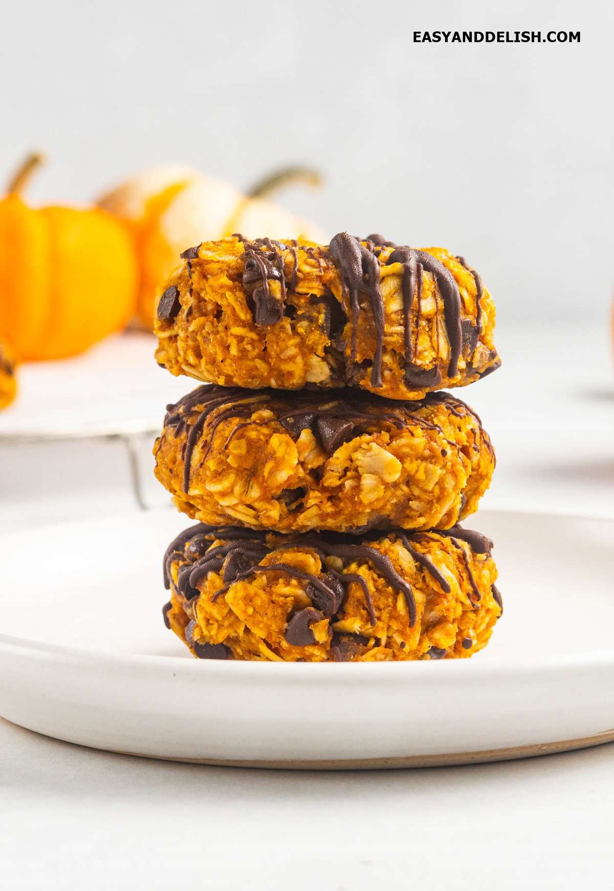 pile of no-bake pumpkin cookies with chocolate drizzlein a plate.