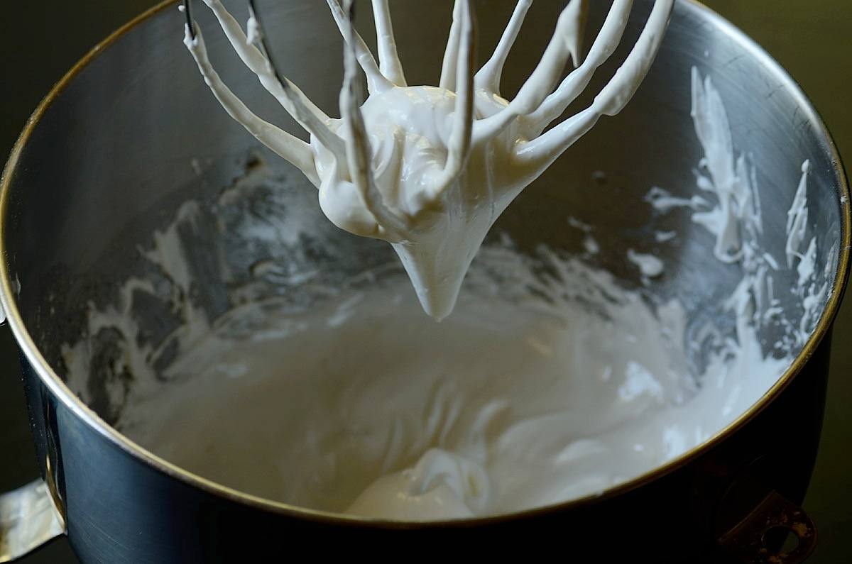 beaten whipped cream hanging on a whisk of a stand mixer.