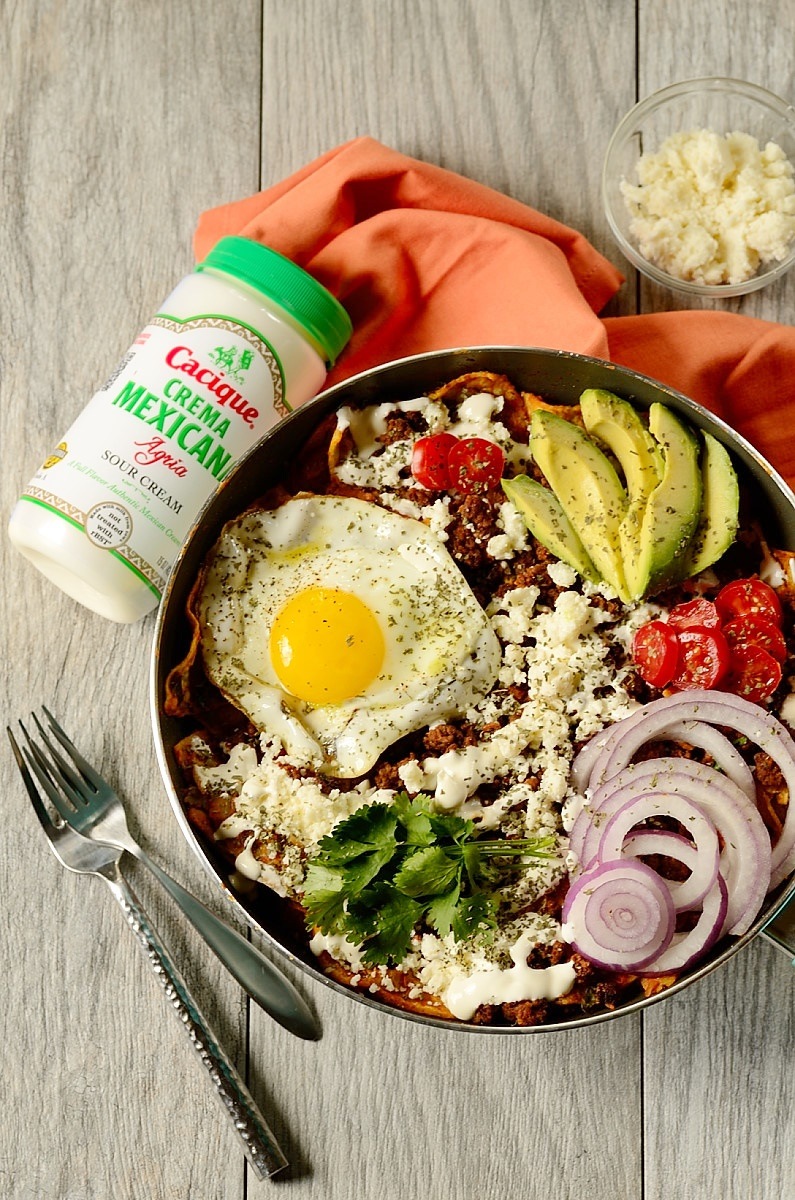 breakfast chilaquiles in a skillet with crema and cheese on the side