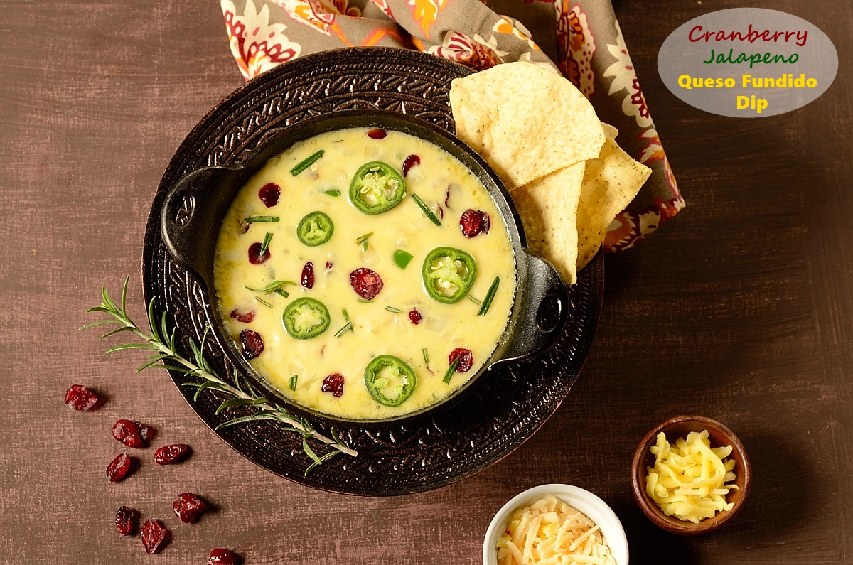 A skillet of queso fundido topped with jalapeno and dried cranberries and chips on the side