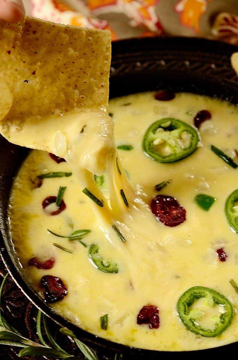 An ooey-gooey, salty-sweet and mildly spicy Cranberry Jalapeno Queso Fundido Dip to serve as an easy appetizer for the holidays. It's low carb, keto, and gluten-free! #glutenfree #lowcarb #keto #easy #quick #quesofundido #dip #appetizer close up image of a tortilla cheese pulling up melted cheese.