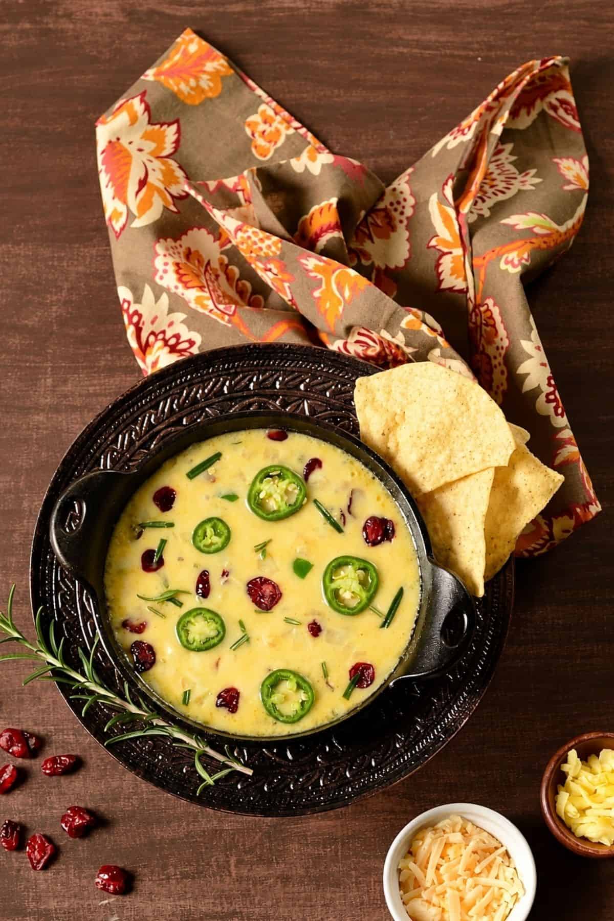 Cranberry jalapeño melted cheese dip in a skillet with tortilla chips and fresh rosemary.