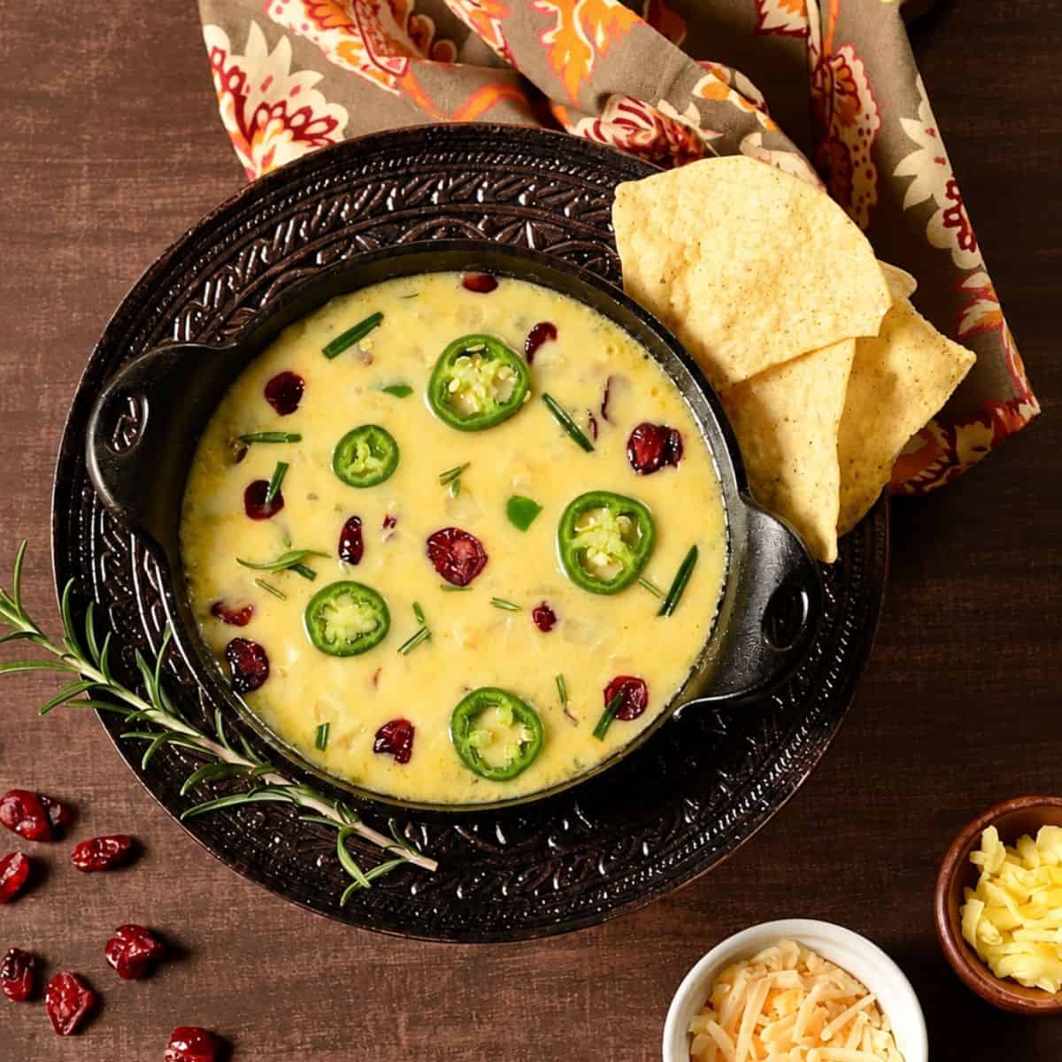 Cranberry jalapeño queso fundido dip served warm in a black skillet with tortilla chips and rosemary.