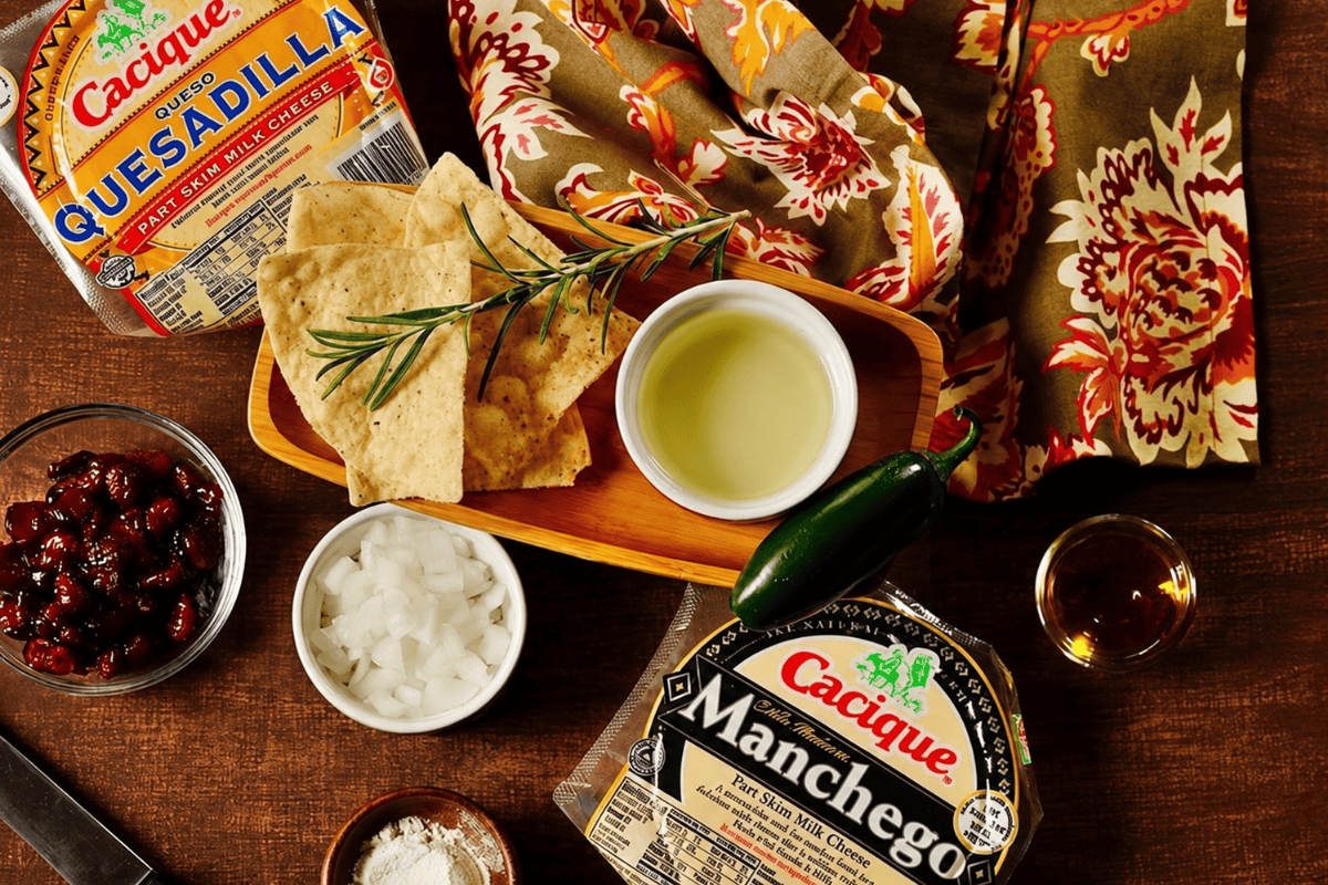 Queso fundido ingredients with Manchego, queso quesadilla, onion, jalapeño, cranberries, rosemary, wine, and tortilla chips.