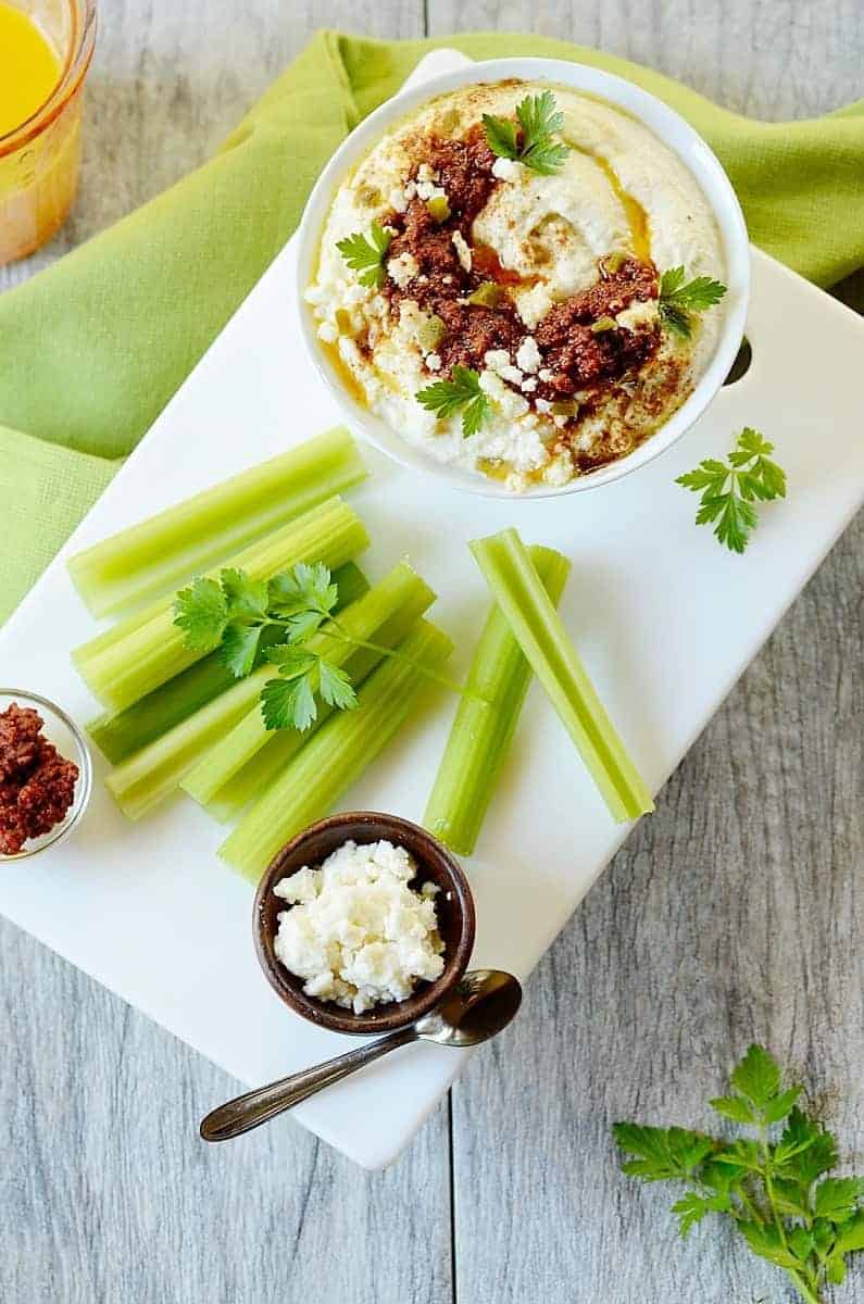 keto hummus topped with cheese and chorizo with celery sticks on the side