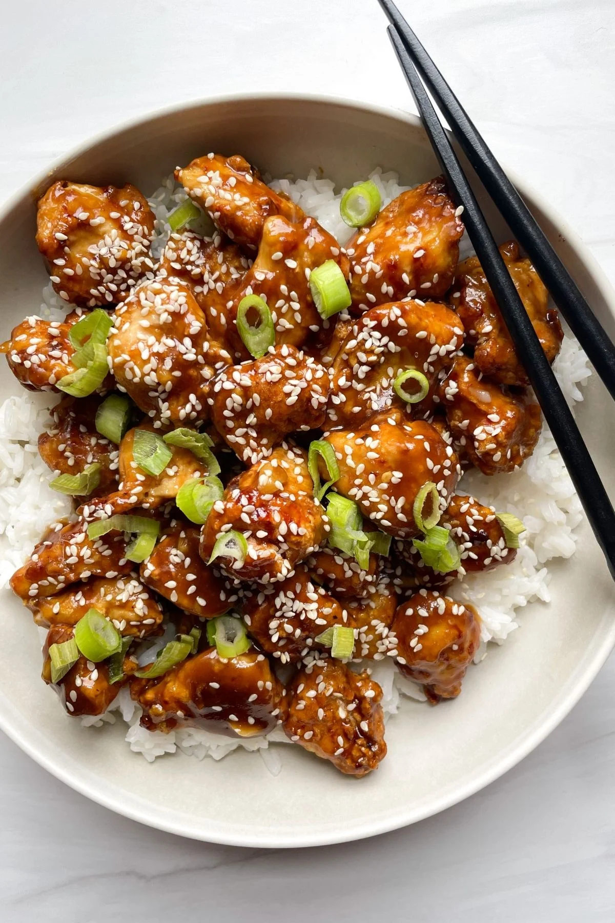 air fryer sesame chicken in a plate with chopsticks on the side -- by Hello Frozen Bananas
