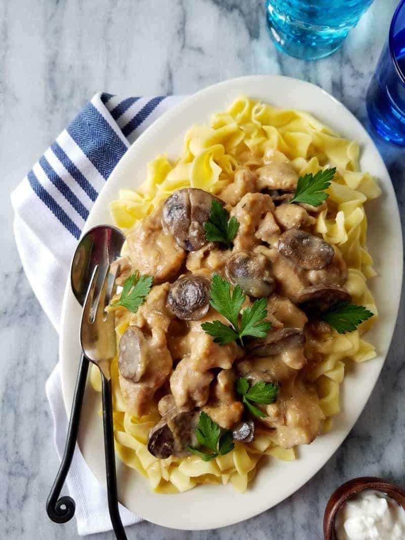 Slow cooker lean pork stroganoff on a plate with a white and blue cloth