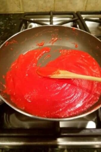 Strawberry brigadeiros mixture being stirred in a pan on the stove with a wood spatula