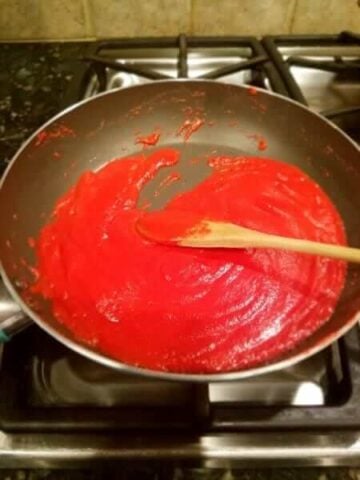 Strawberry brigadeiros mixture being stirred in a pan on the stove with a wood spatula