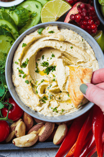 keto hummus made with cauliflower and pita chips dipped in it with a hand.