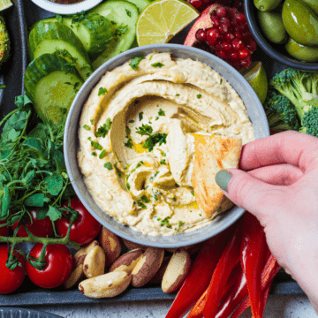 keto hummus made with cauliflower and pita chips dipped in it with a hand.
