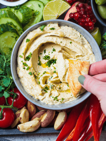 keto hummus made with cauliflower and pita chips dipped in it with a hand.