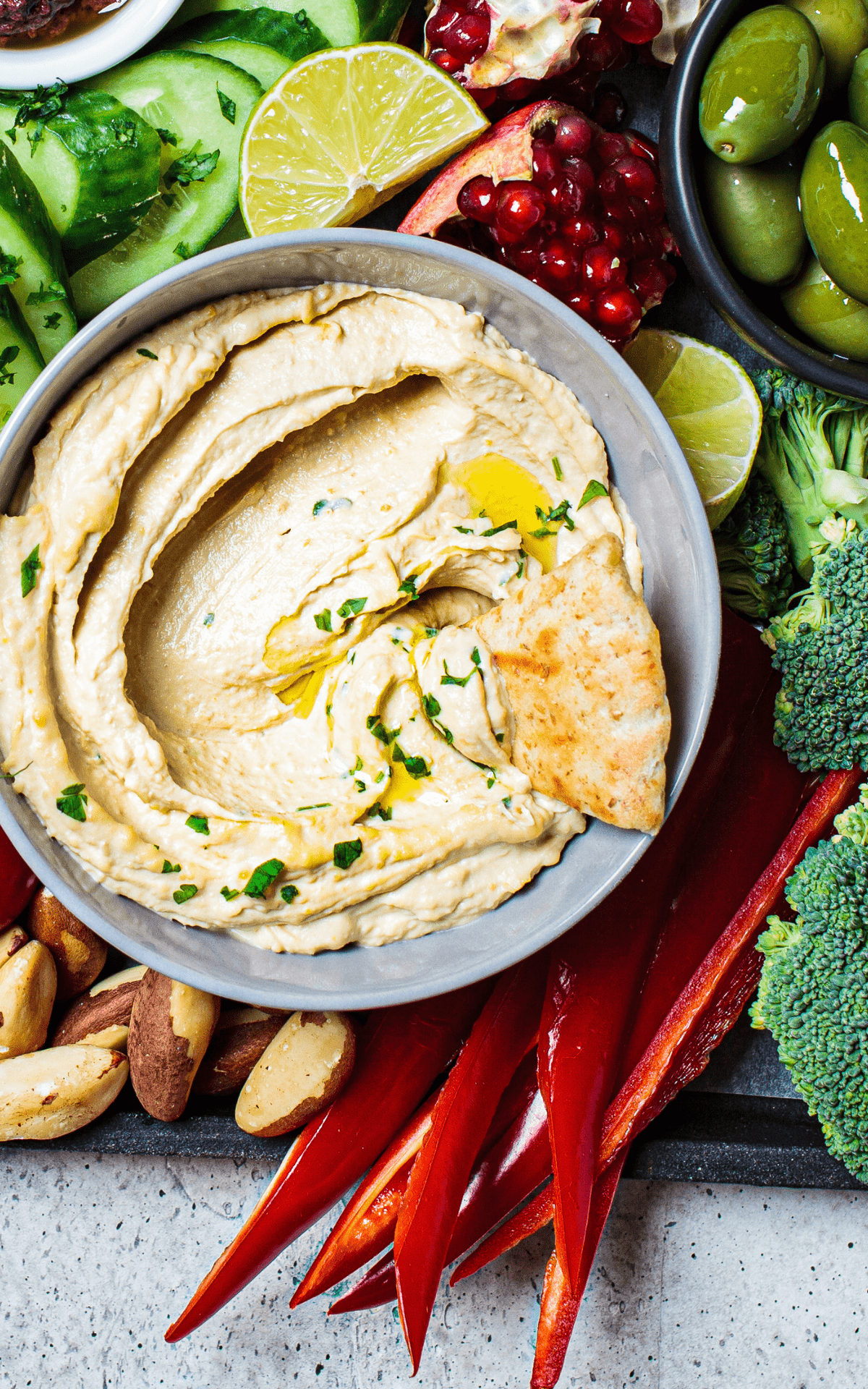 pita chips dipped in a bowl of creamy cauliflower hummus  with crudites around it.