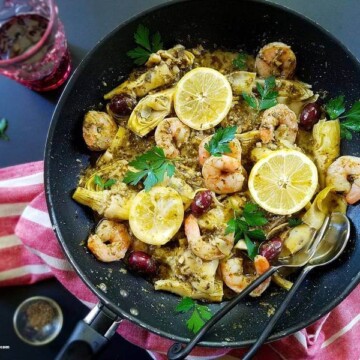 a pan of seafood with pesto sauce and a glass of wine on the side