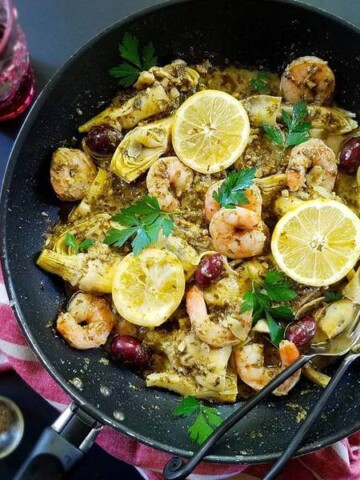 a pan of seafood with pesto sauce and a glass of wine on the side