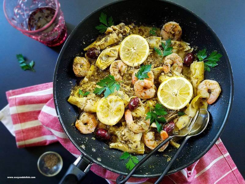 a pan of seafood with pesto sauce and a glass of wine on the side