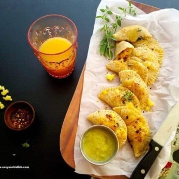 A plate of chicken empanadas with a glass of juice on the side