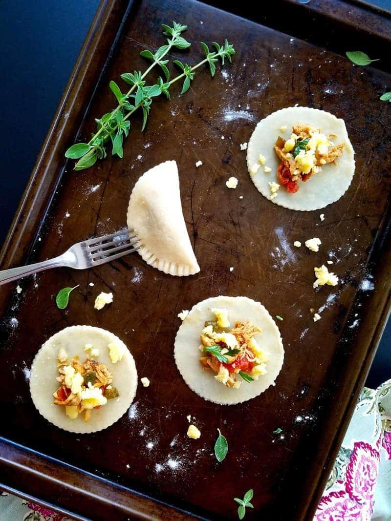 folding chicken empanadas in a baking sheet