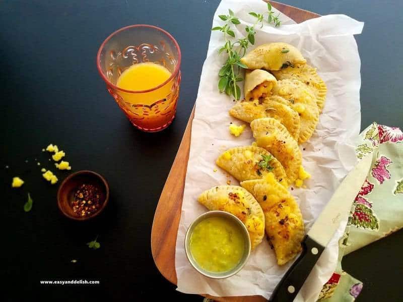 A plate of chicken empanadas with a glass of juice on the side