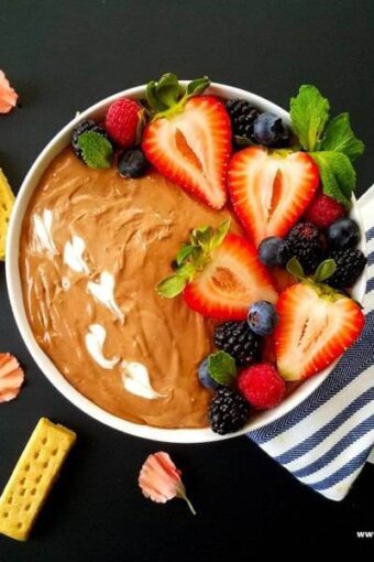 A bowl of Nutella dip topped with berries and cookies of the side