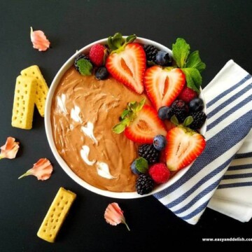 A bowl of Nutella dip topped with berries and cookies of the side
