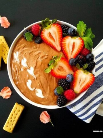 A bowl of Nutella dip topped with berries and cookies of the side