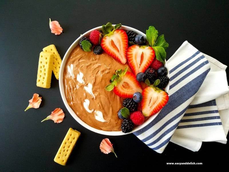 A bowl of Nutella dip topped with berries and cookies of the side