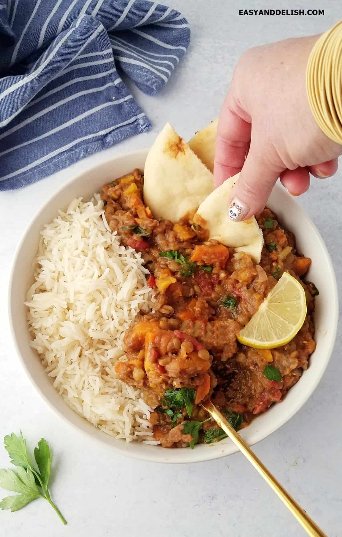 A piece of naan dipped into Moroccan lentil stew served in a bowl of rice. 