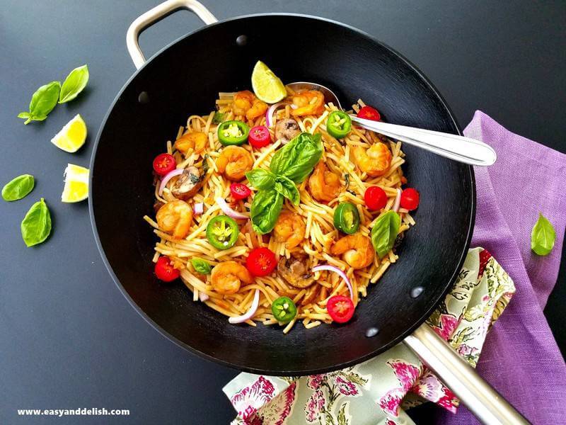 shrimp noodles in a wok with lime wedges on the side