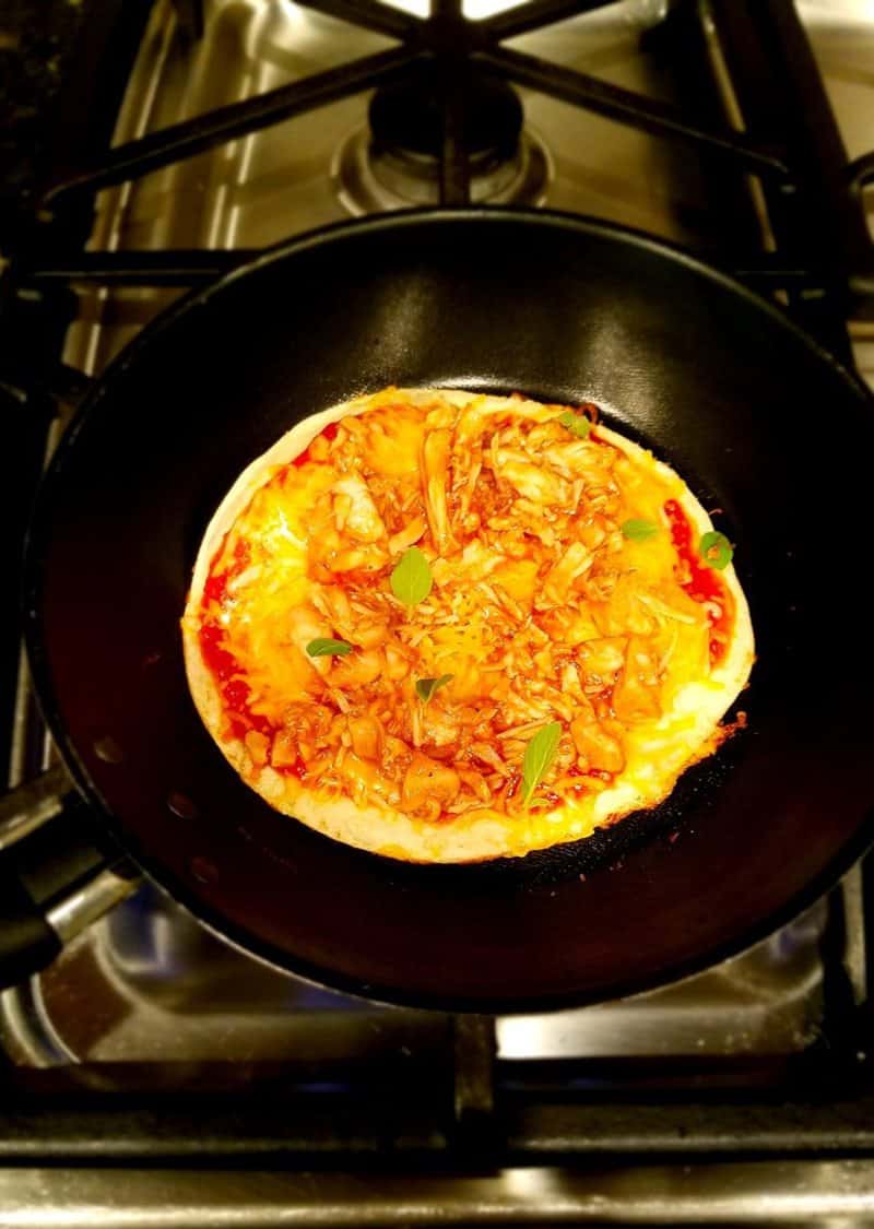 tortilla in a pan topped with sauce and shredded chicken
