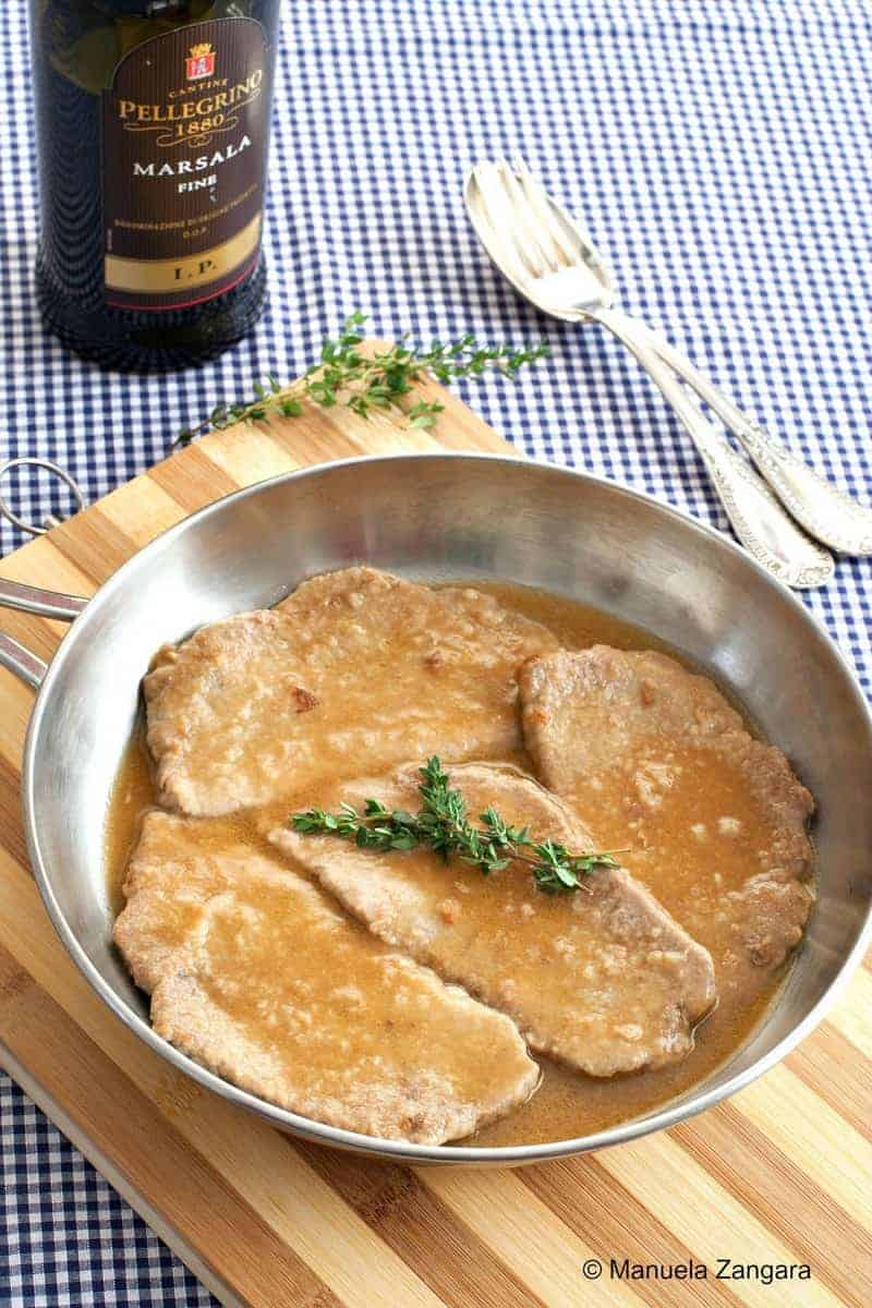 Scallopine al Marsala in a skillet with a bottle of Marsala wine on the background. 