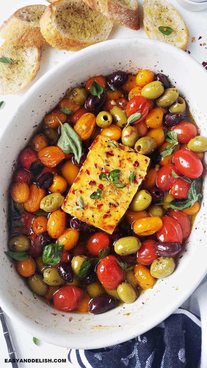 Greek appetizer warm with tomatoes, olives, herbs, olive oil and honey after coming out of the oven with crostini on the side