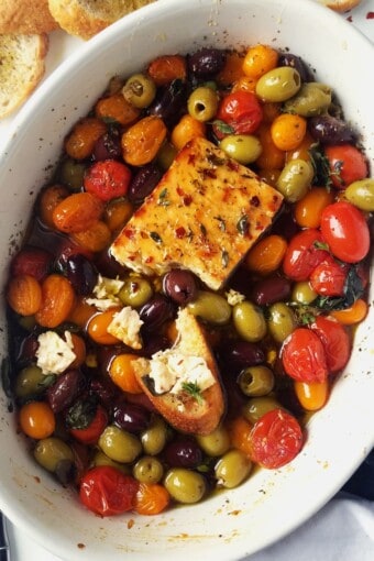 a baking dish with baked feta, roasted Greek veggies, and crostini