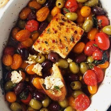 a baking dish with baked feta, roasted Greek veggies, and crostini