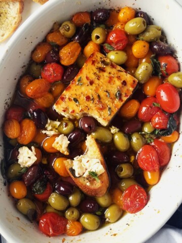 a baking dish with baked feta, roasted Greek veggies, and crostini