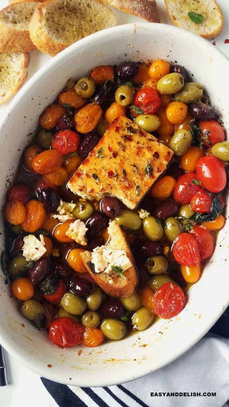 a baking dish with baked feta, roasted Greek veggies, and crostini