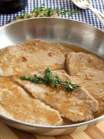 A skillet with veal marsala garnished with fresh herbs on top.