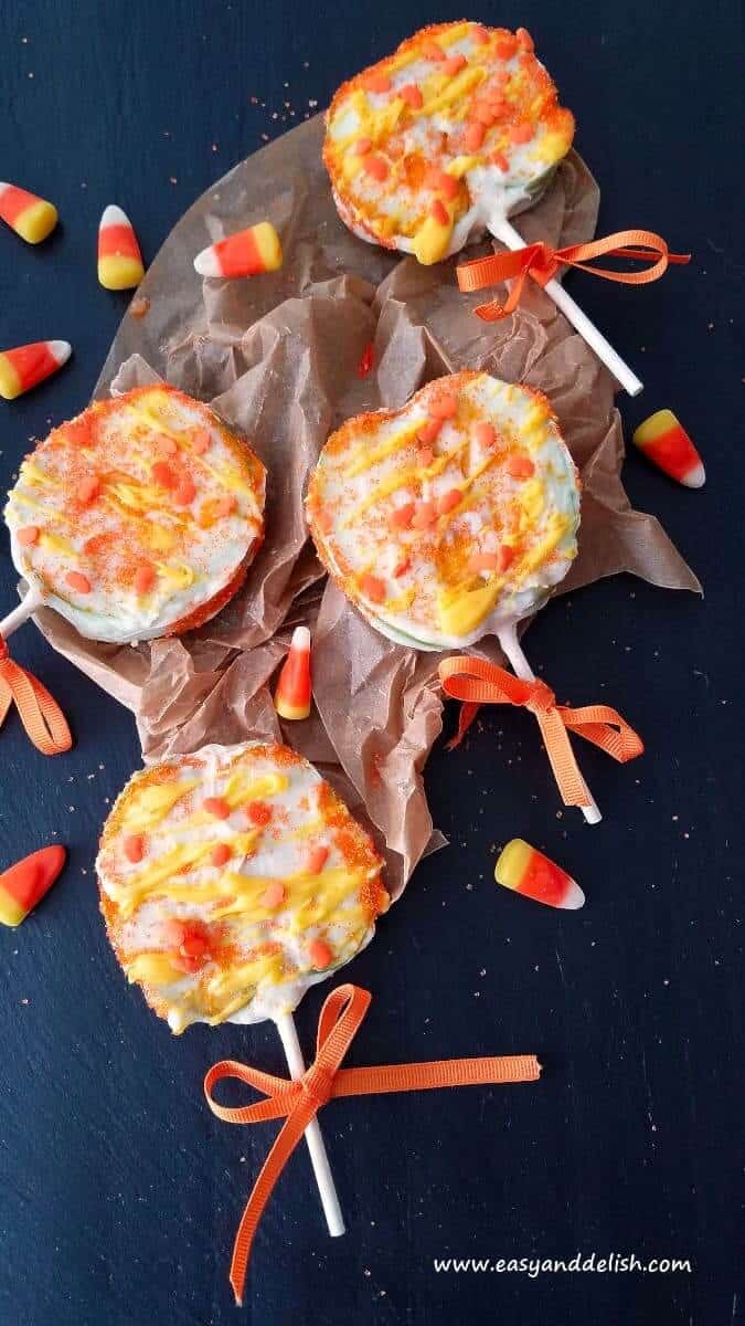 4 candy corn apple pops over a table with candy corns all around