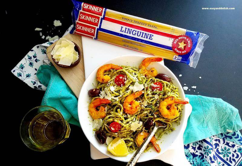 a bowl of pasta with shrimp and vegetables with a package of dry pasta on the background